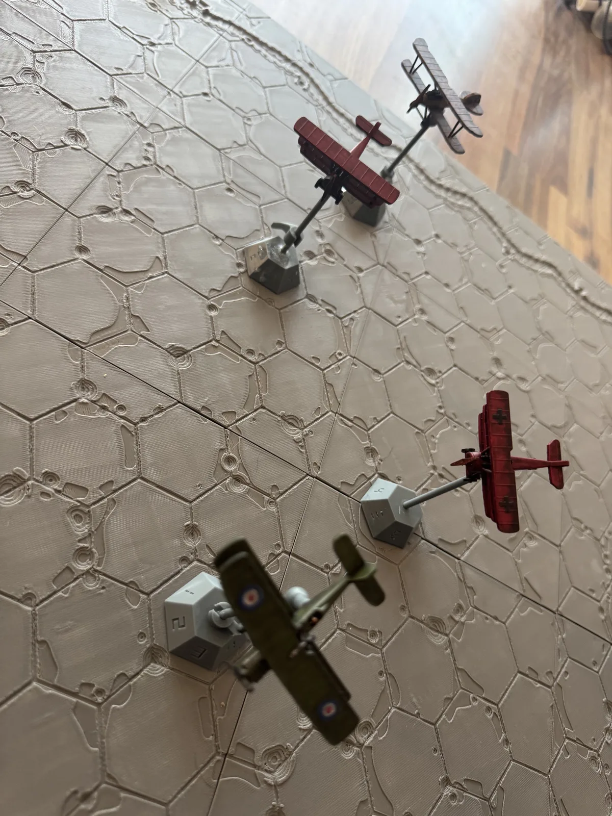 Painted WWI aircraft on HexAxis stands flying over a printed Death Spiral Battlefield during a prototype test